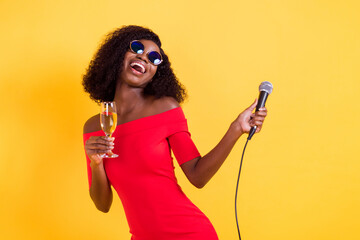 Sticker - Photo of young happy excited laughing afro girl drinking champagne hold microphone isolated on yellow color background