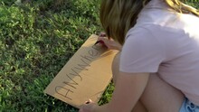 The Girl Writes Anywhere With A Marker On Cardboard. Hitchhiking. Trying To Stop The Car With A Sign