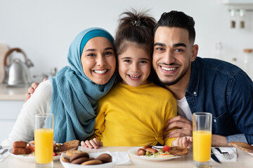 Wall Mural - Happy Islamic Parents With Little Daughter Posing In Kitchen, Having Lunch Together