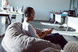 © Wavebreak Media - Smiling african american businesswoman sitting in armchair, wearing headphones, using smartphone