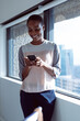 © Wavebreak Media - Smiling african american businesswoman standing at window, using smartphone