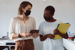 © Wavebreak Media - Two diverse businesswomen wearing face masks, holding tablet and documents, talking