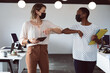 © Wavebreak Media - Two diverse businesswomen wearing face masks, holding tablet and documents, touching elbows