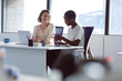 © Wavebreak Media - Two diverse businesswomen sitting at desk, talking and smiling