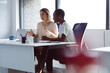© Wavebreak Media - Two diverse businesswomen sitting at desk, looking at laptop, talking