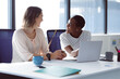 © Wavebreak Media - Two diverse businesswomen sitting at desk, talking and smiling