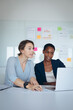 © Wavebreak Media - Two diverse businesswomen sitting at desk, using laptop, talking