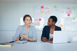 © Wavebreak Media - Two diverse businesswomen sitting at desk, using laptop, talking