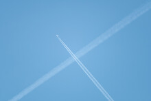 Low Angle Shot Of Intersecting Plane Trails In The Blue Sky Forming An "X".