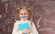 Funny grimacing  little girl in glasses near chalkboard full of signs and formulas. Education concept.