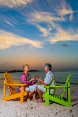 Wall Mural - Romantic older couple at the beach with beach chairs having drinks, champagne, at sunset