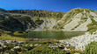 Taul Tapului glacial lake in a sunny summer day.  The lake has a small island in one of its sides. The rocky glacier cauldron is located in Retezat Mountains, Romania
