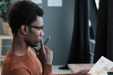 Wall Mural - African student in eyeglasses sitting with pensive look and preparing for exams