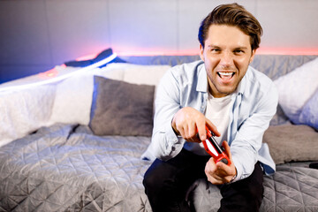 Joyful young Caucasian male playing game at home on console station. Smiling millennial man gamer having fun enjoy world of videogames, cyber sport activity on weekend