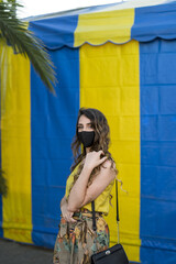 Wall Mural - Positive young female in a medical face mask standing and posing at camera in the park