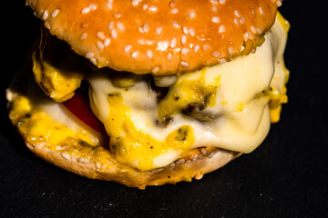 Poster - High angle shot of a tasty beef cheeseburger with melted cheese isolated on black background