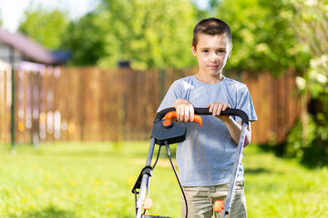 Portrait a boy  with an electric lawn mower mowing the lawn.Beauty boy  pruning and landscaping a garden, mowing grass, lawn, paths.