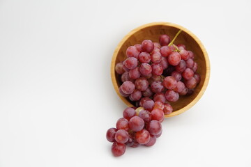 Fresh and ripe red grapes in a wooden bowl, isolated in white background. Bunch of raw and juicy grapevines