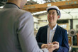 © twinsterphoto - 30s young Asian businessman in formal suit and hard hat showing foreign business partner in factory background. Business partnership and team work success concept