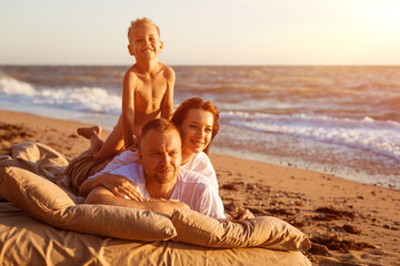 Wall Mural - Dad tosses his son up. Lie on a bed by the sea at sunset. Family vacation on the sandy beach. Young family have fun on summer vacation.