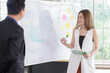 © DUSITARA STOCKER - Happy business people in meeting with colleagues, businesswoman writing business plan on white board , present with businessman, working together in office workplace