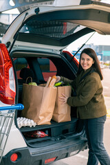 Wall Mural - woman put bags with products in car trunk after grocery store