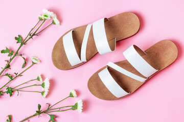 A pair of white sandals and flowers on pink background top view.