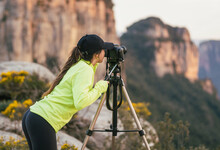 Young woman photographing mountains on camera placed on tripod