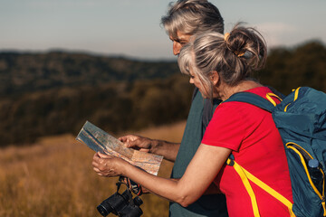 Wall Mural - Active senior couple hiking in nature with backpacks, enjoying their adventure at sunset.