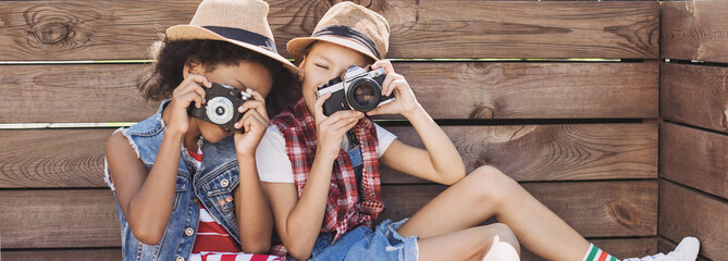 Wall Mural - Two little girls outdoor portrait. Diverse multi ethnic kids friends playing together, taking pictures with photocameras. Summer fun, friendship, diversity, vacations concept