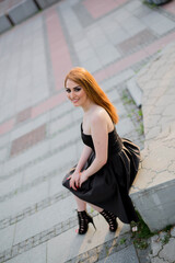 Sticker - Young attractive woman in a black dress sitting on the stone and posing