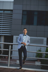 Wall Mural - Young handsome elegant man in a blue suit and bow leaning on a railing