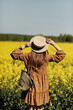 Rear view. beautiful young woman in a dress holding a hat and walking in a rapeseed field for summer, view from the back. copy space. summer holiday concept