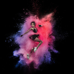 Wall Mural - Young sportsman, female athlete running in explosion of colored powder explosion isolated on black background