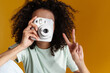 Young african curly woman showing peace sign while taking photo on camera