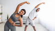 Millennial black couple doing lateral flexion exercise, working out together at home during coronavirus quarantine