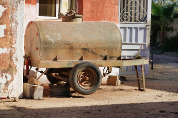 Poster - A side view of old rusty metal barrel trailer put outside next to the building