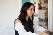 © Lea - Smiling woman using laptop while sitting on chair in living room. Young woman working  in home office in front of a computer