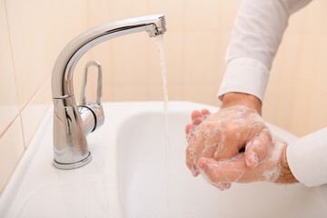 hand washing with soap or gel under running water in the washbasin, cleanliness and hygiene, men's hands dressed in a white shirt