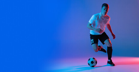 Flyer. Young Caucasian man, male soccer football player training isolated on gradient blue pink background in neon light