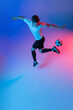 © master1305 - High angle view of young man, male soccer football player training isolated on gradient blue pink background in neon light.