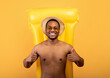© Prostock-studio - Top view of happy black man lying on inflatable lilo and showing thumbs up with both hands, yellow background