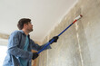 Caucasian man painting cement walls using roller brush and primer making a renovation.