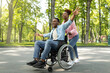 Happy black disabled guy in wheelchair on walk with his loving girlfriend outdoors, having fun, spending time together