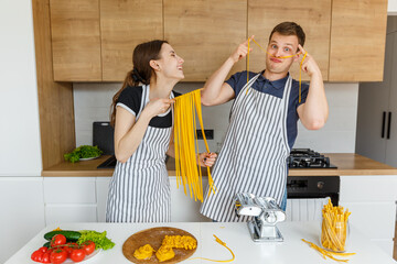 Young couple in aprons having fun with pasta noodles. Family cooking italian vegan food at home. Concept of domestic lifestyle, healthy eating, happy marriage and togetherness