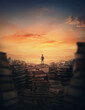 Surrealistic scene with a tiny man climbing on the top of a huge books landfill. Different thrown book piles and a person silhouette against sunset. Educational concept, in search of knowledge