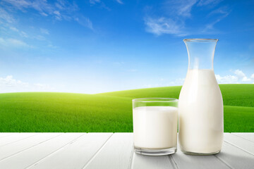 Wall Mural - Glass and bottle of fresh milk on white wooden table with green meadow background.