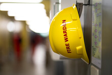 A Yellow Safety Helmet For "Fire Warden" Is Hanging On Wall In The Building, Standy By For Use In Fire Emergency Case. Industrial Safety Object Close-up Photo.