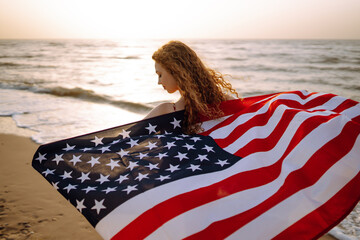 Young woman with american flag on the beach at sunset. 4th of July. Independence Day. Patriotic holiday.