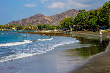 Beautiful beach with dark sand, Bali sea in the background on sunny summer day in Pemuteran, north Bali coastline, Indonesia